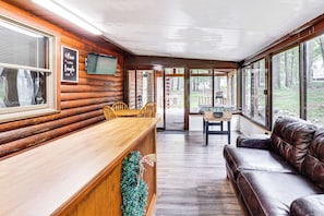 L’intérieur d’une cabane en rondins, avec un bar en bois, un canapé en cuir et un coin repas comprenant une table et des chaises.