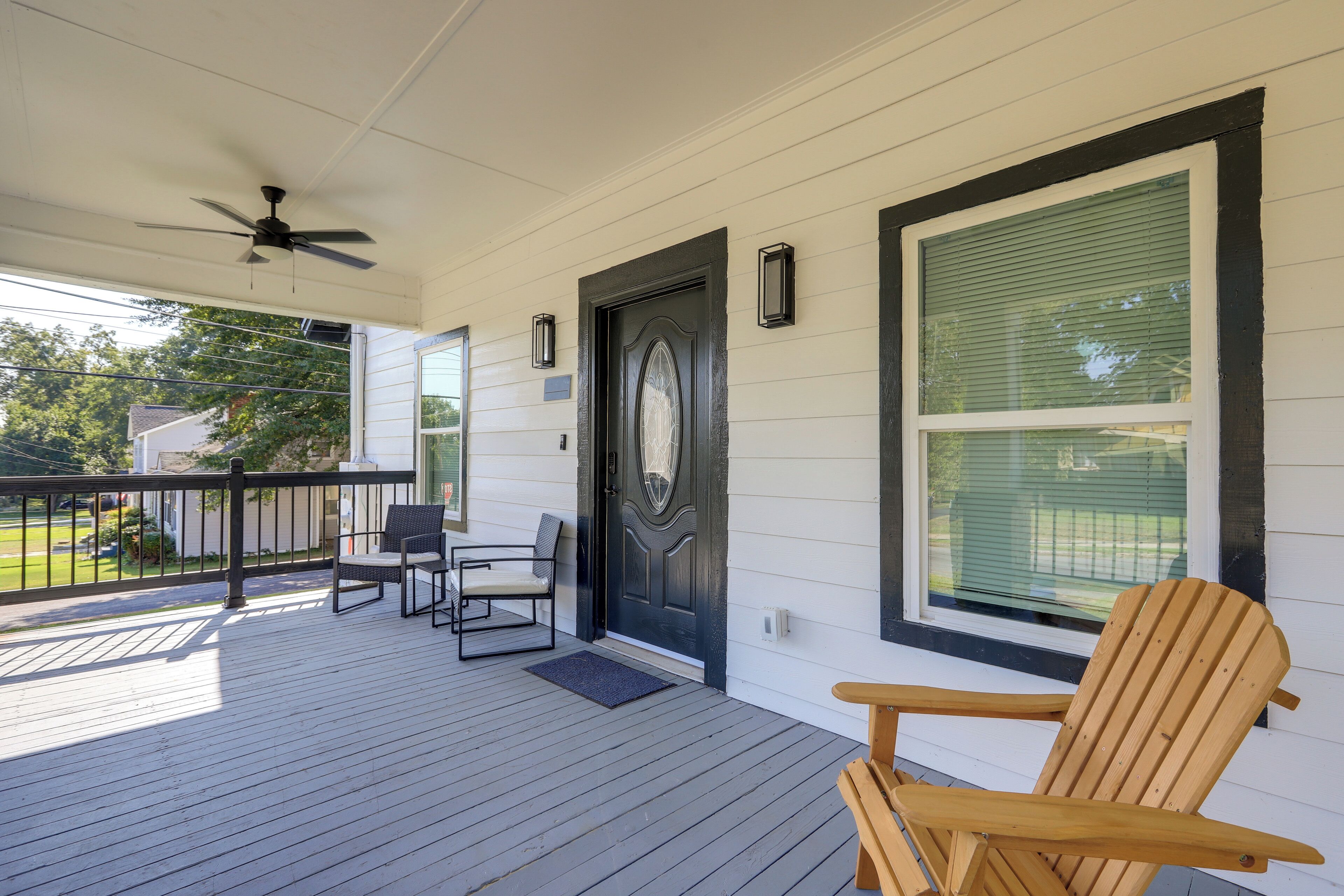 A wooden deck with a ceiling fan, a dark door, and two windows with blinds.