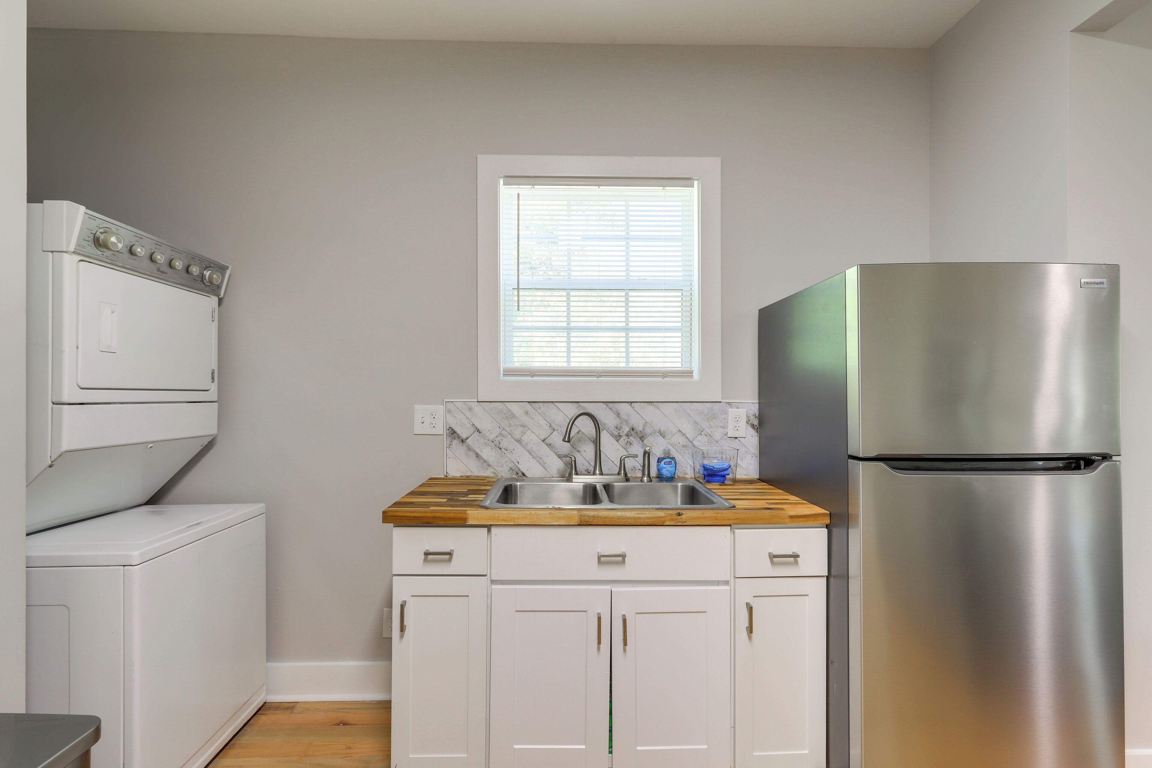 A compact kitchen with a built-in oven, a stainless steel refrigerator, a wooden countertop, and a window with blinds.