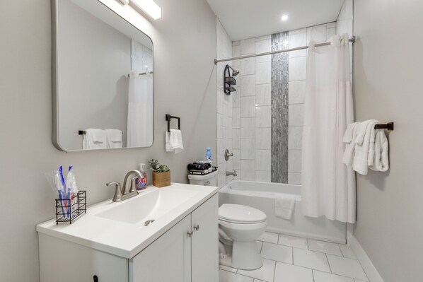 A modern bathroom with a white sink, mirror, toilet, and shower area.