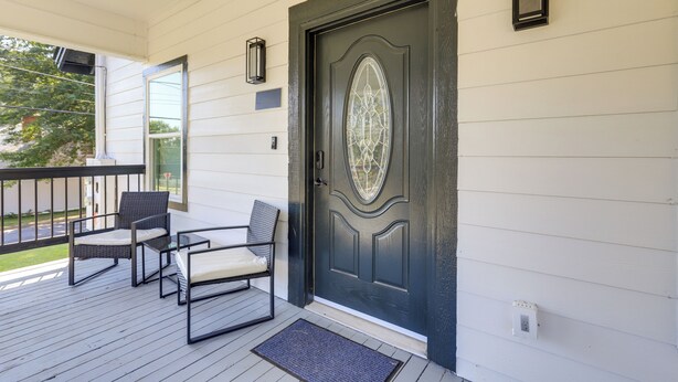 A porch with a dark door, two wicker chairs, a small table, and a ceiling fan.