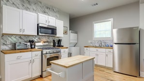A modern kitchen with white cabinets, a wooden countertop, stainless steel appliances, and a marble backsplash.