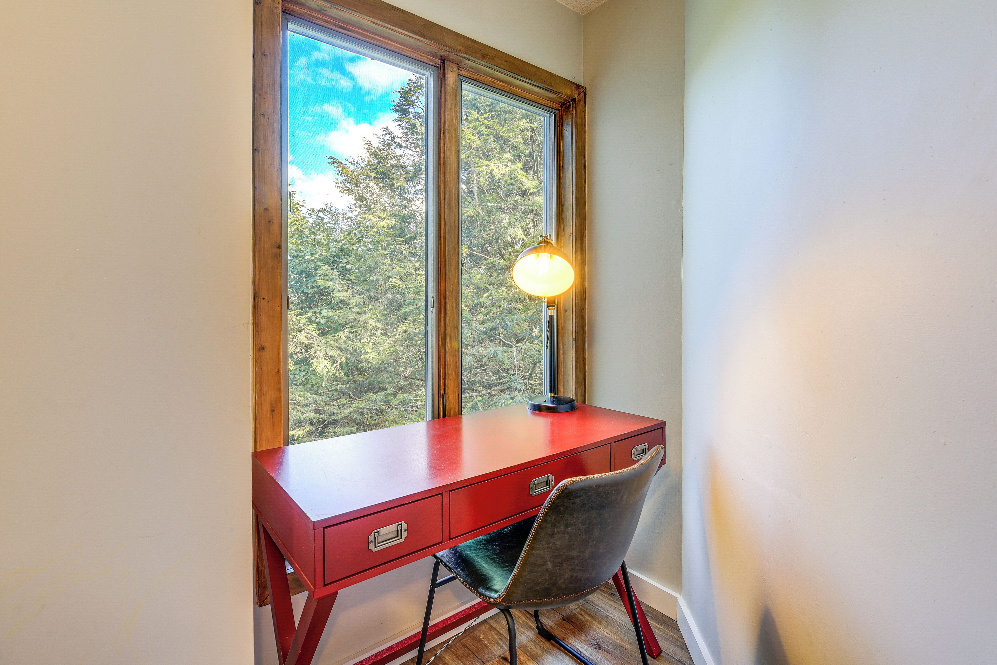 Een rode bureau met een lamp, geplaatst bij een raam met uitzicht op bomen.