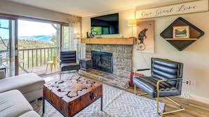 A living room with a stone fireplace, a mounted TV, and a view of the outdoors. - Families Welcome! Sugar Mtn Gem: Golf, Hike & Ski (Banner Elk)