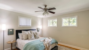 A bedroom with a bed, a ceiling fan, two windows, a bedside table, and a floor lamp. - < 1 Mi to Ole Miss & The Grove! Charming Getaway (Oxford)
