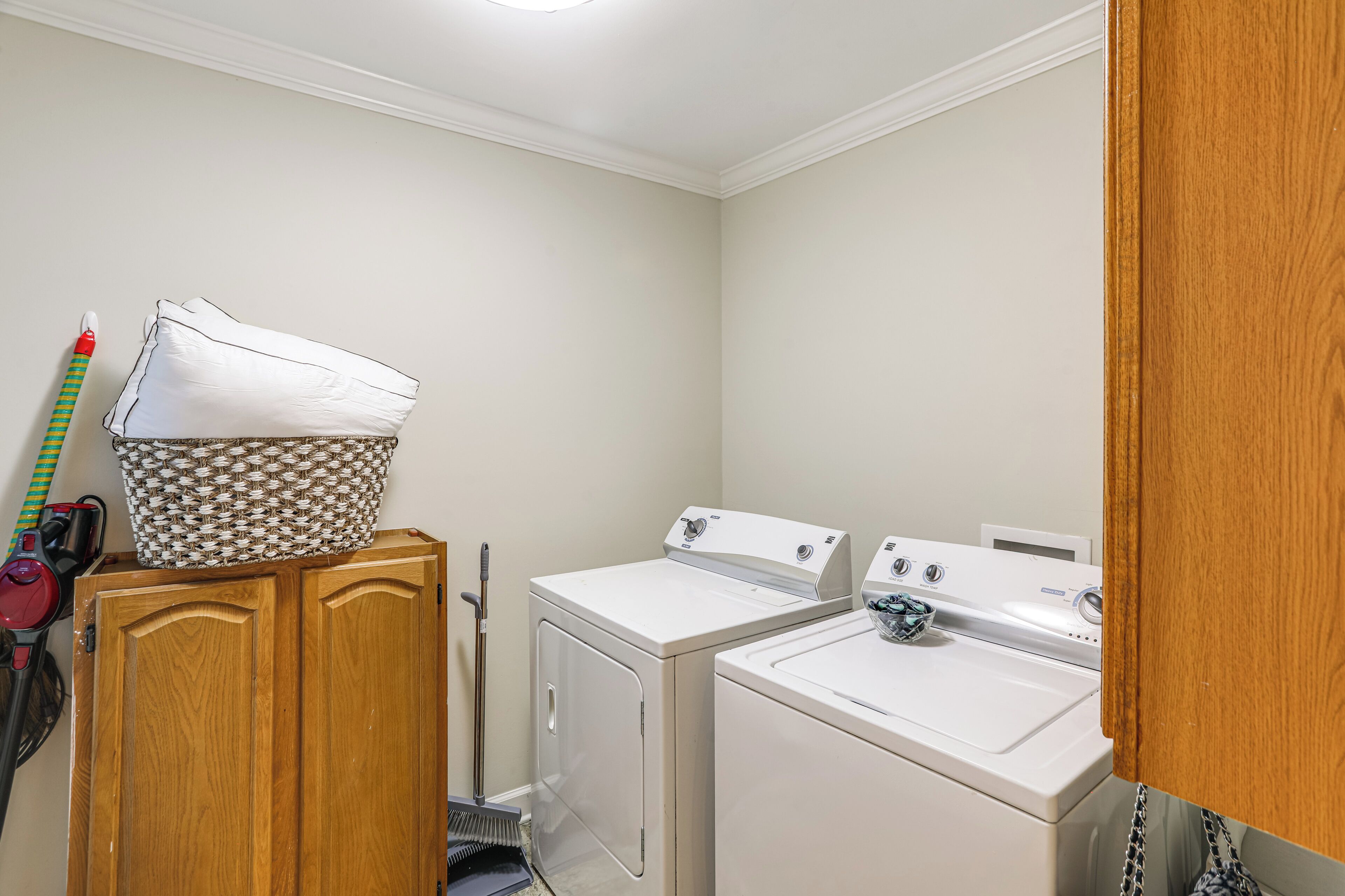 A laundry room with two washing machines, a wooden cabinet, and a basket on top.