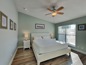 A bedroom with a bed, nightstands, a ceiling fan, and a window with blinds.