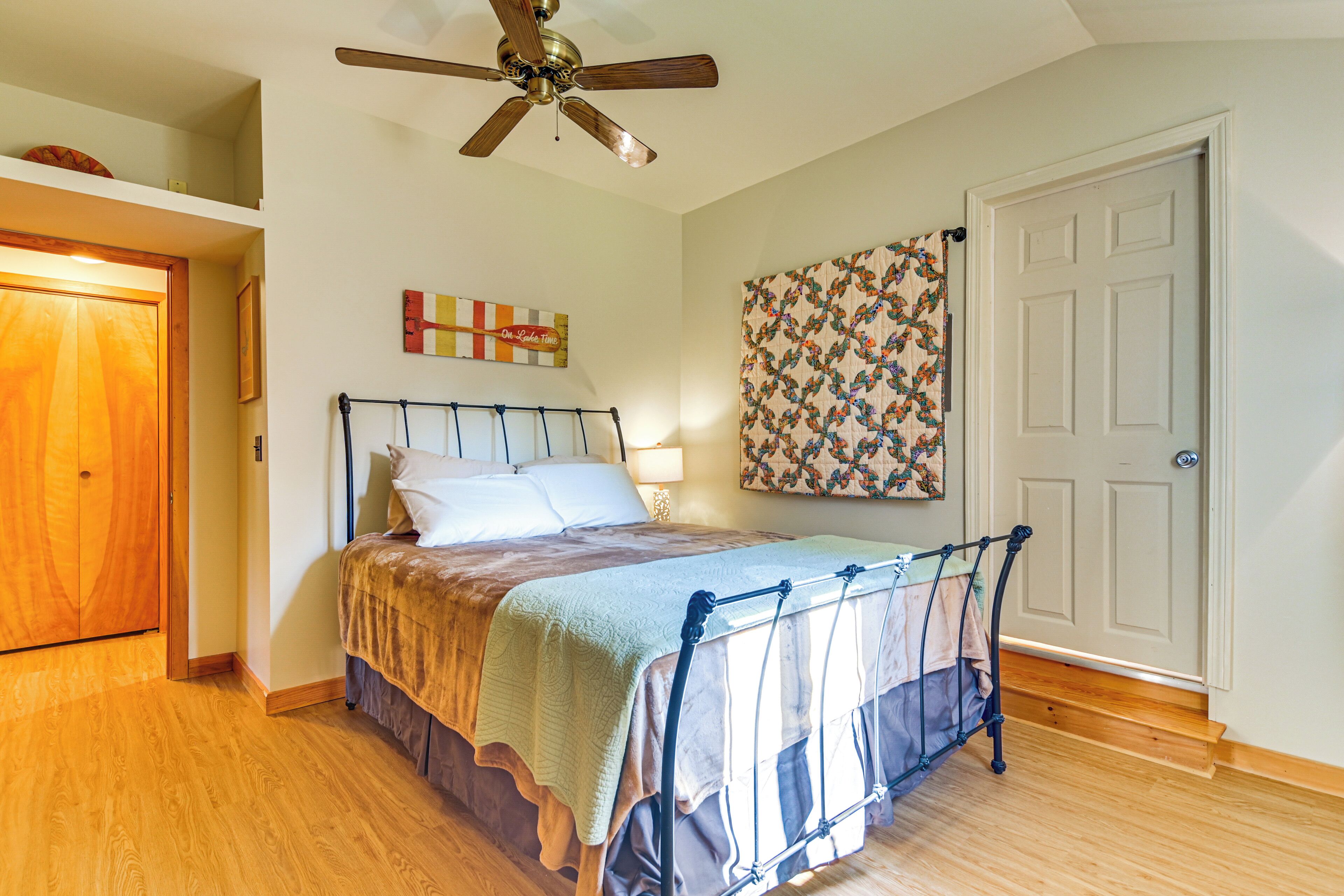 A bedroom with a bed, wooden floor, ceiling fan, and a door.