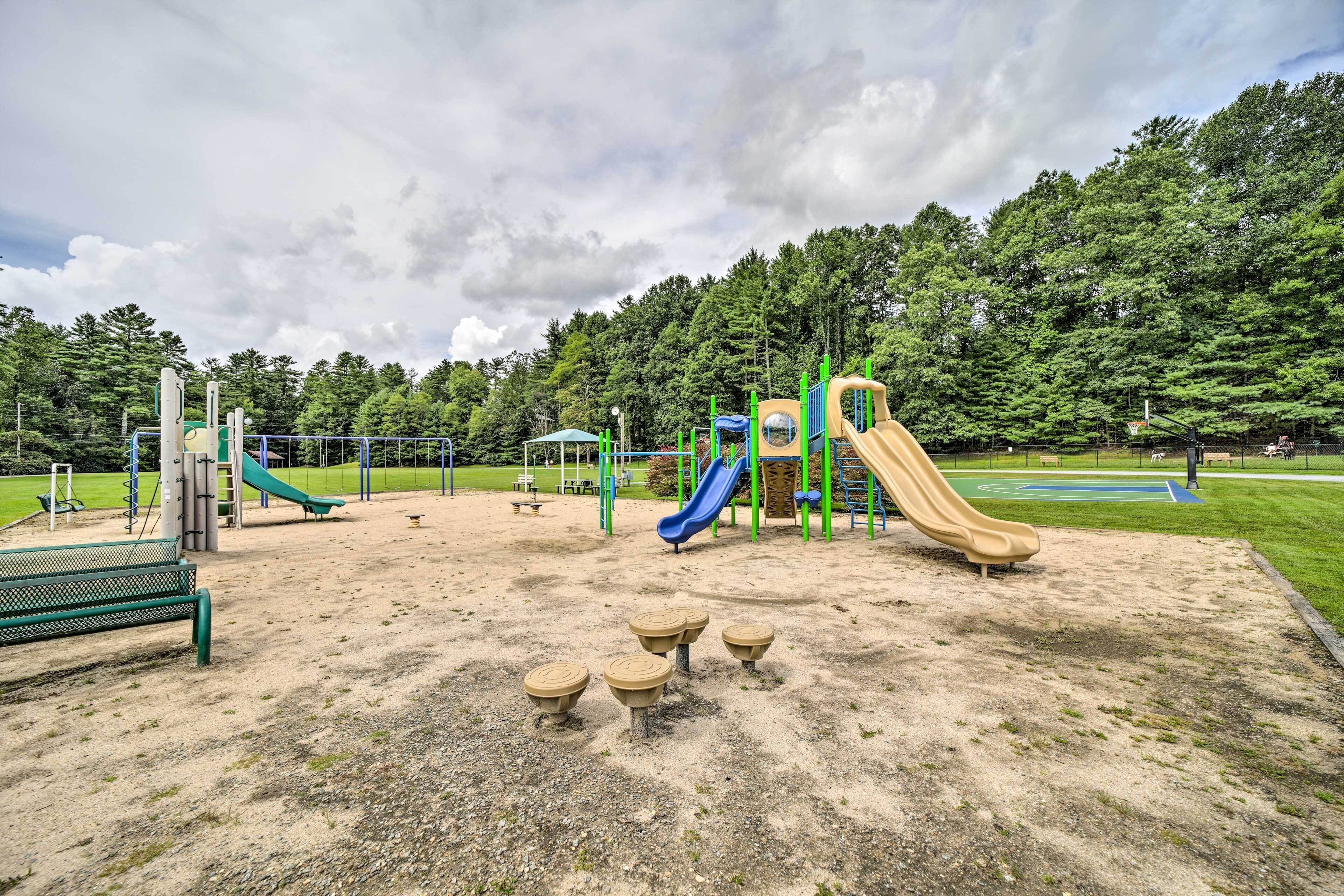 Un parque infantil con toboganes y estructuras para escalar, rodeado de césped y árboles.
