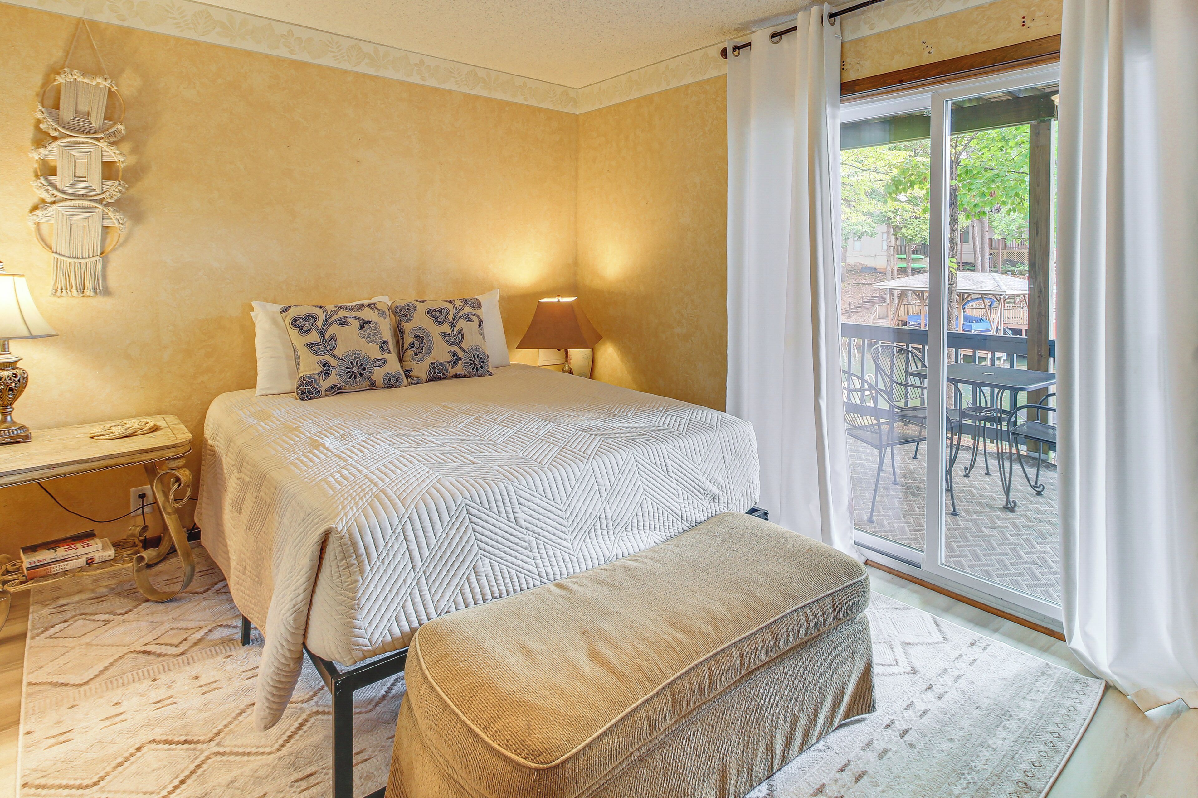 Un dormitorio con cama, mesita de noche, lámpara y vistas a un patio exterior con sillas y mesas.