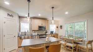 A modern kitchen with a central island, wooden cabinets, and pendant lighting. - Lake Access, Pools & More: Family Home in Stanwood (Stanwood)