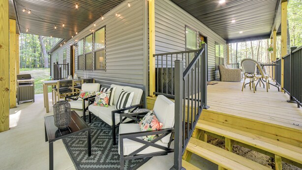 A covered outdoor patio with a wooden deck, a sofa, chairs, and a table. - Lake Access, Pools & More: Family Home in Stanwood (Stanwood)