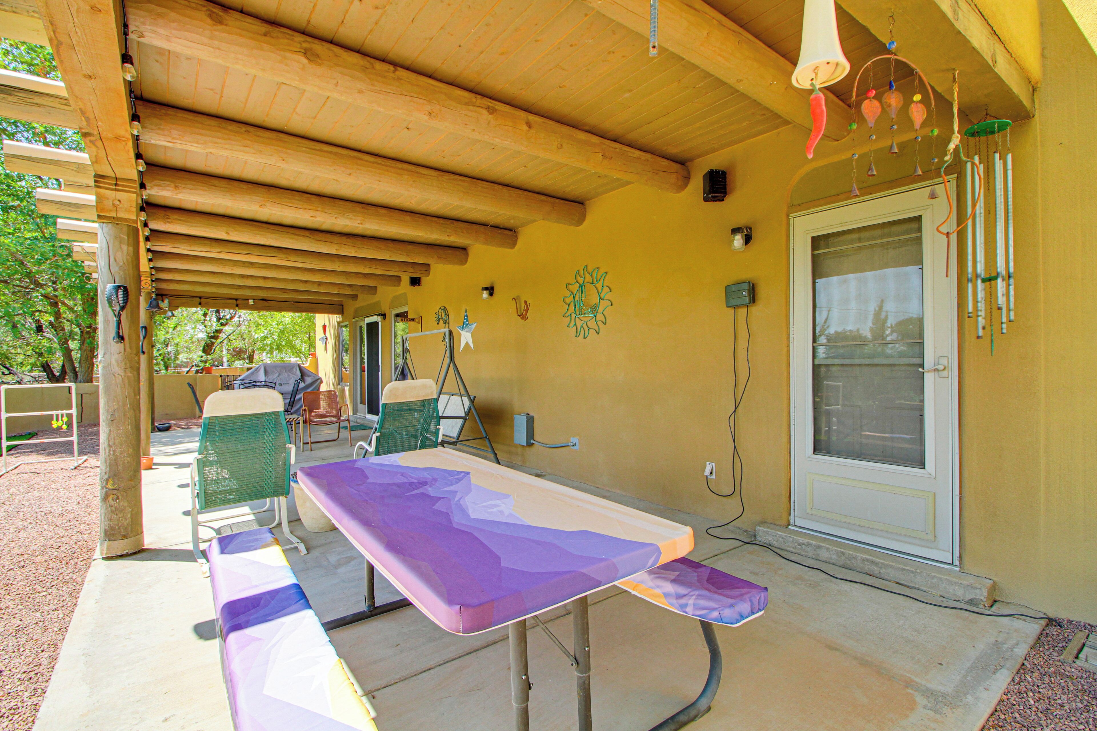 An outdoor covered patio with a long table and chairs, wooden beams, and a door with a window.