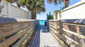 Une promenade en bois qui mène à une plage bordée de palmiers, sous un ciel bleu et dégagé.