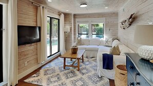 Un vaste espace de vie doté d’un plafond en bois, d’un téléviseur à écran plat fixé au mur, d’un canapé blanc, d’une table basse en bois et d’un tapis à motifs.