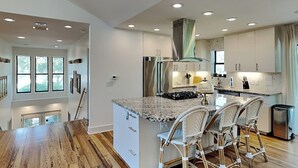 Une cuisine moderne dotée d’un îlot central, de meubles blancs et d’une hotte de cuisine en acier inoxydable.