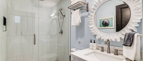 A modern bathroom with a glass-enclosed shower, a white sink with a vanity, and a decorative mirror.