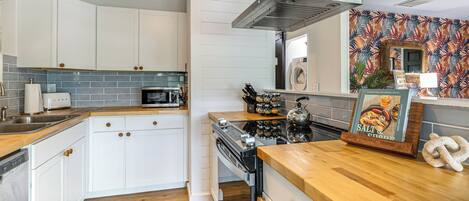 A modern kitchen with white cabinets, a microwave, a stove, and a wooden countertop.