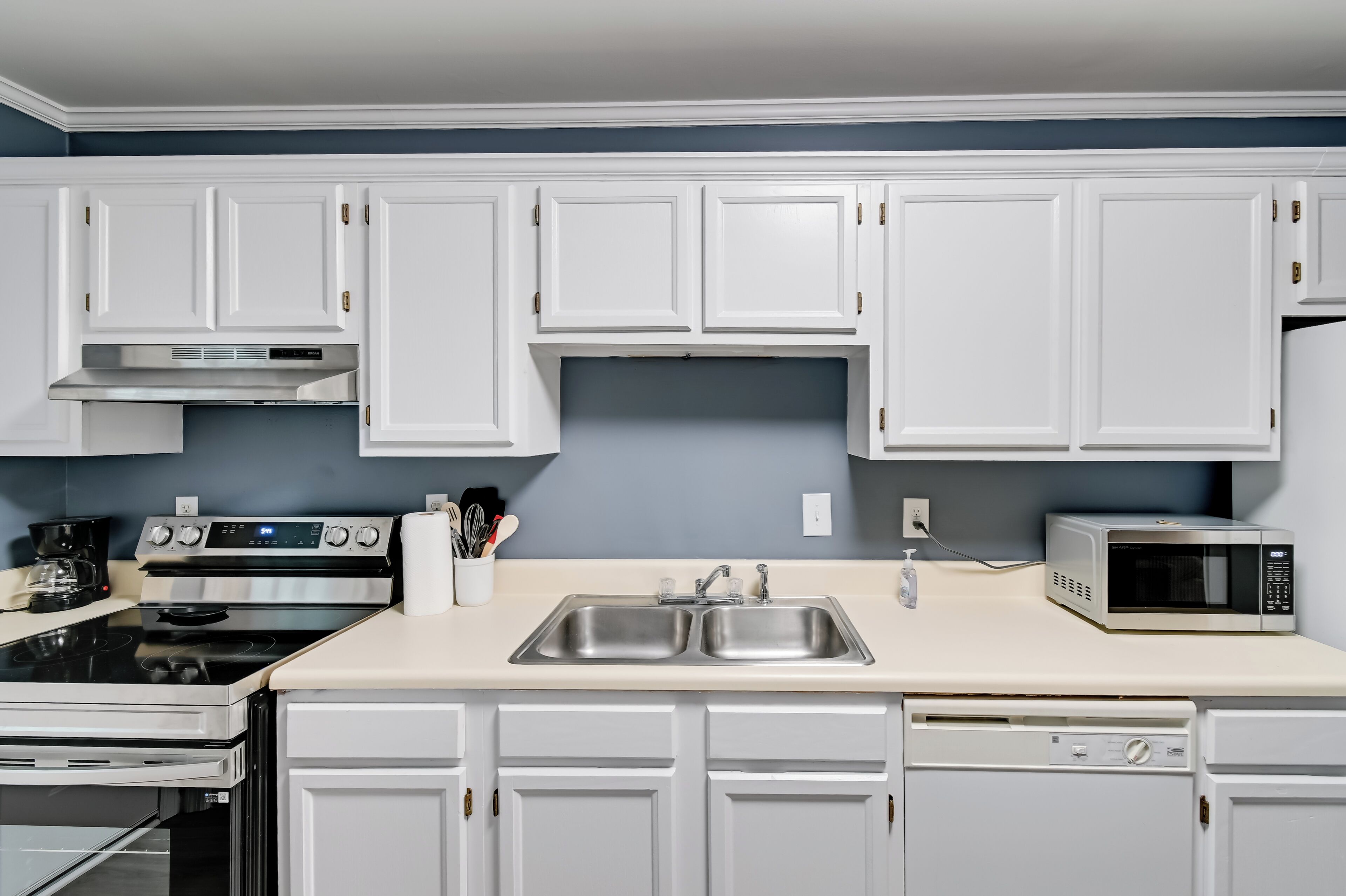 A kitchen with white cabinets, a double sink, a stove, a microwave, and a dishwasher.
