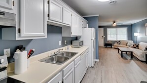 A modern kitchen with white cabinets, a microwave, and a sink. There is a dining area with a sofa and a table. - Private Patio: Apt 6 Mi to Cheraw State Park! (Cheraw)