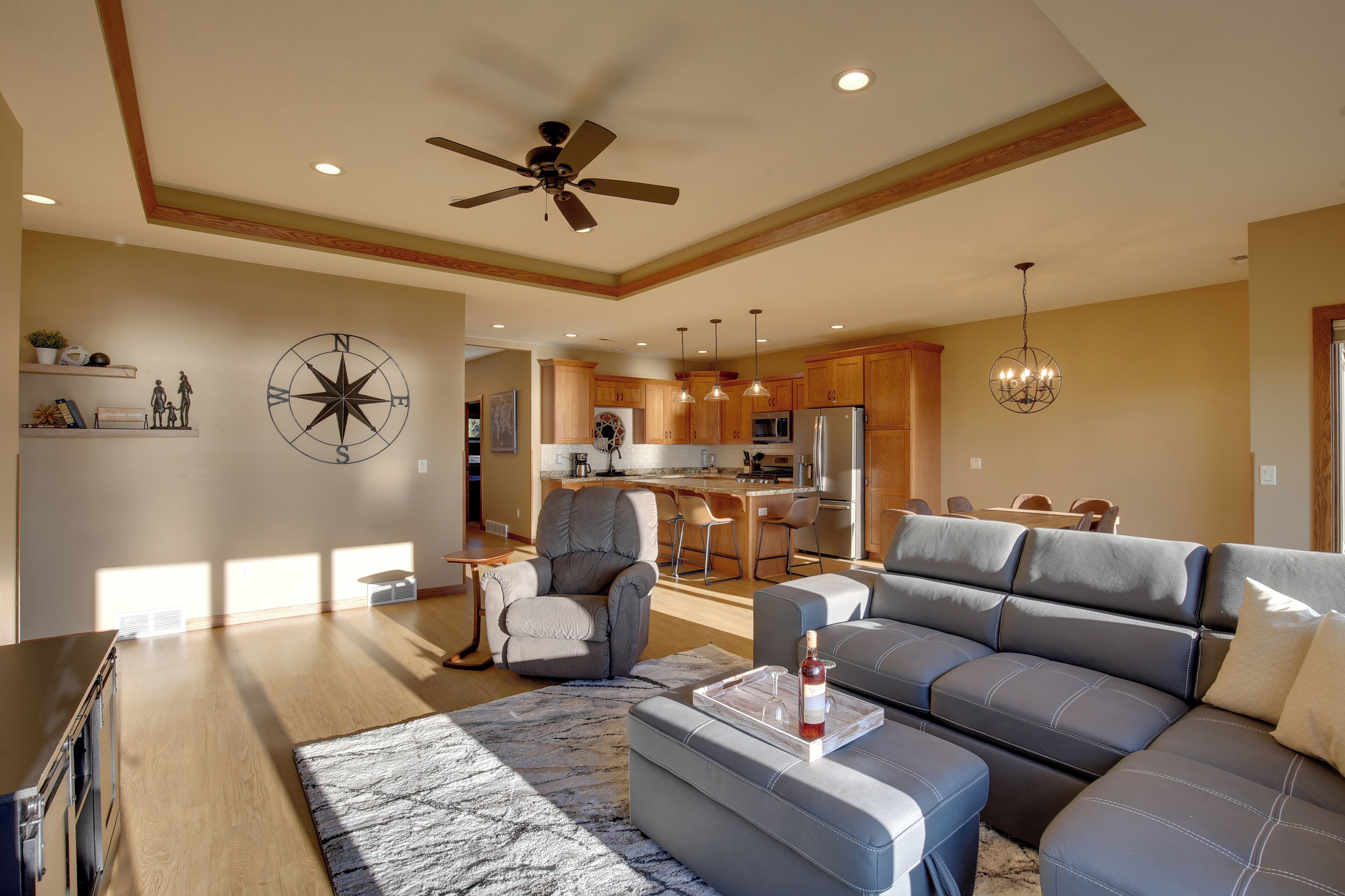 A modern living room with a large sectional sofa, a ceiling fan, and a kitchen in the background.