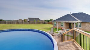Ein Garten mit Schwimmbad, einer Holzterrasse und einem Haus mit Ziegelverkleidung.