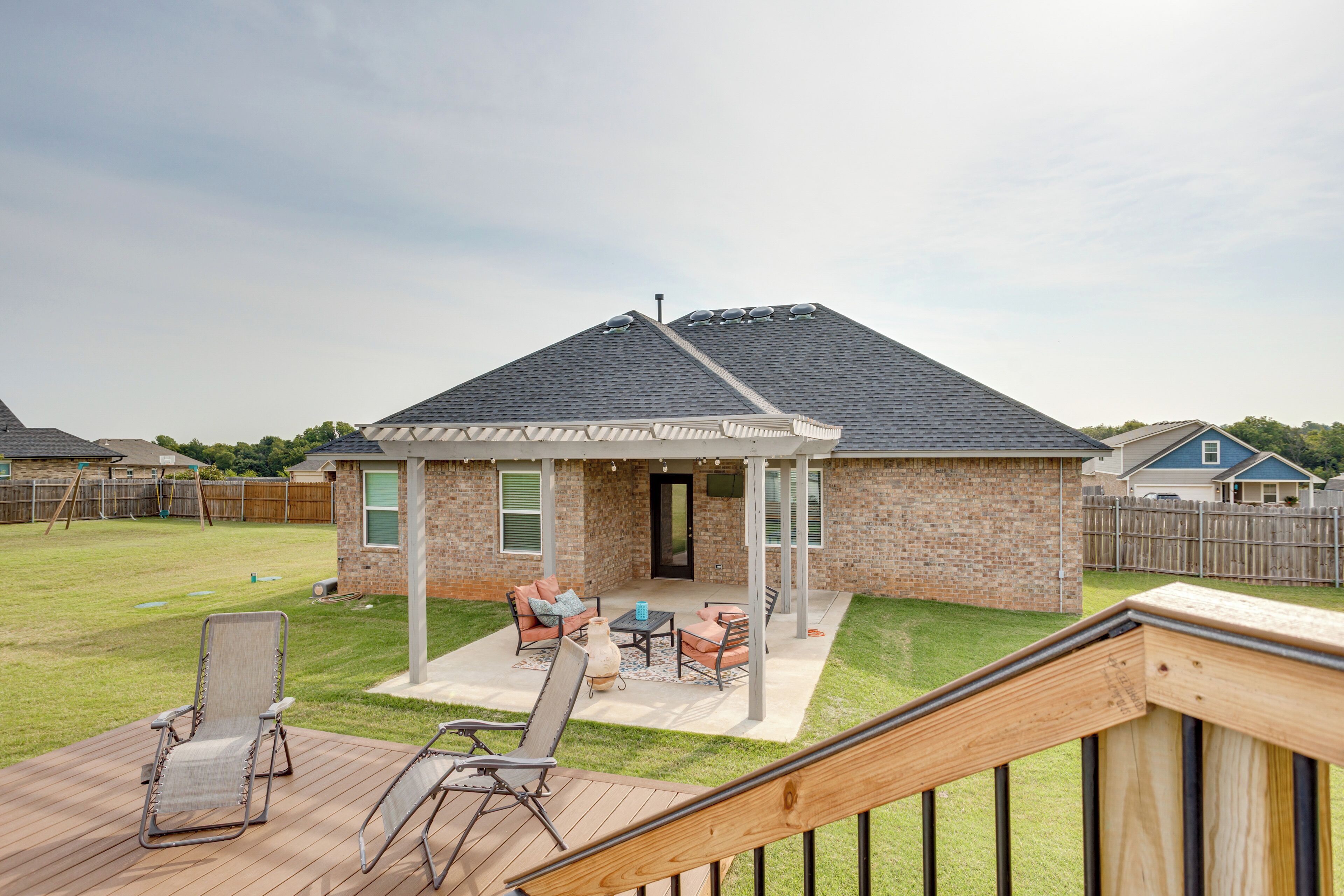 Un jardin avec un patio couvert, une terrasse en bois et une maison en briques.
