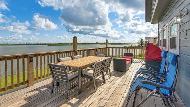 A wooden deck with a table and chairs, overlooking a body of water.