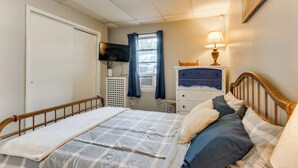 Un dormitorio con cama, televisor, lámpara y ventana con cortinas.