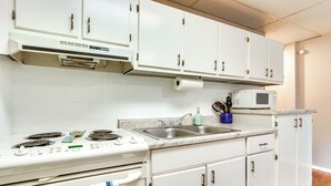 Una cocina con gabinetes blancos, estufa, microondas y lavamanos.