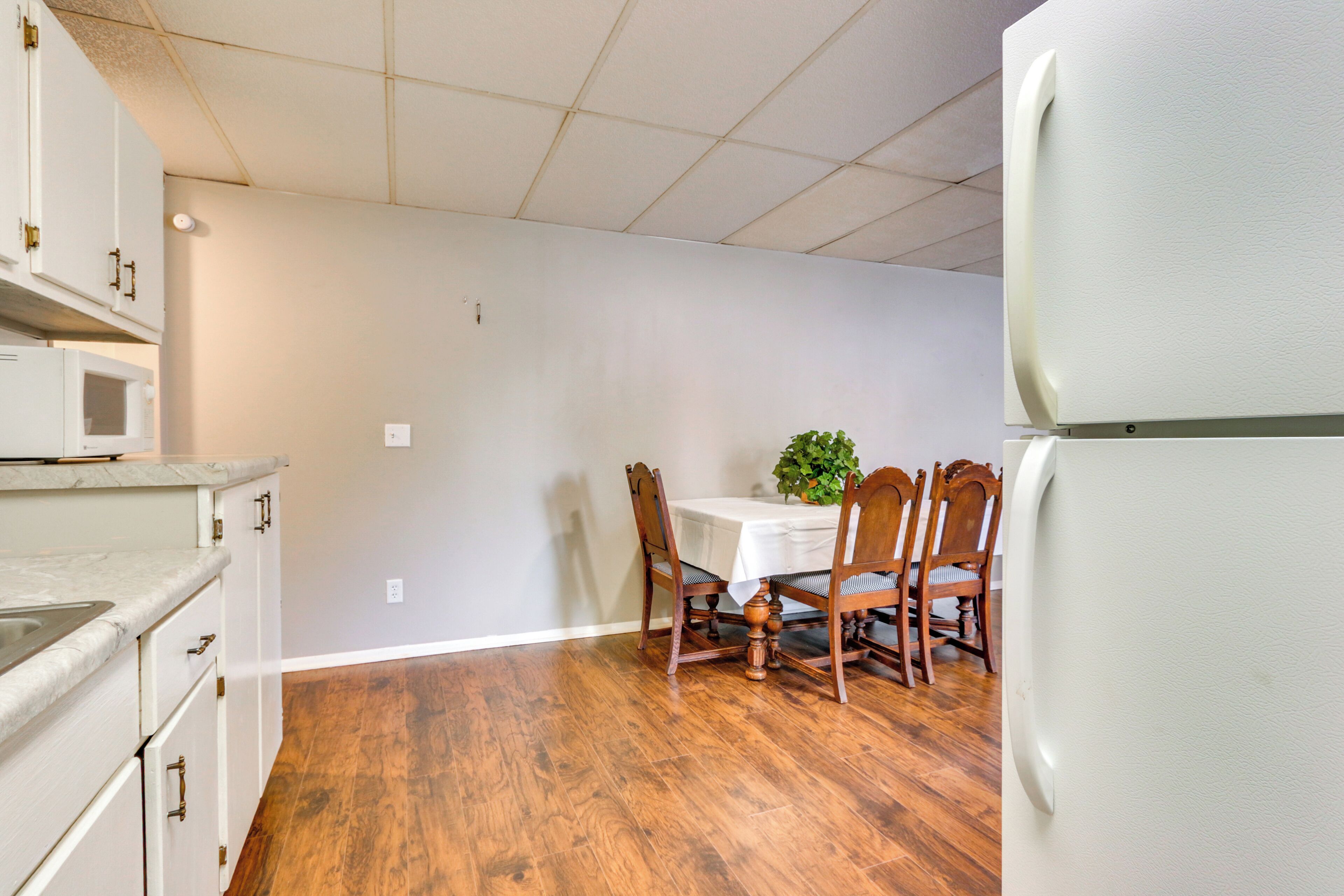 A kitchen with white cabinets, a wooden dining table with chairs, and a white refrigerator.