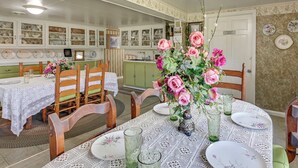 Un comedor con una mesa redonda dispuesta para cuatro personas, rodeada de sillas de madera. Un centro de mesa floral decora la mesa, y hay copas de vidrio verde y platos blancos con motivos florales.