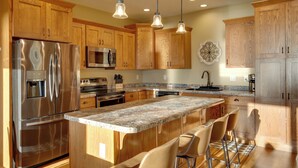 A modern kitchen with wooden cabinets, stainless steel appliances, and a granite island with bar stools. - Game Room + Views: Family Retreat on Silver Lake (Lake Park)