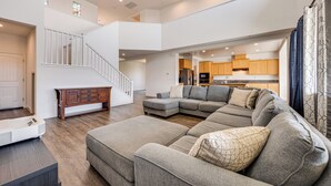 A spacious living area with a large sectional sofa, a wooden cabinet, and a staircase leading to an upper level. - 1 Mi to Golf! Spacious & Modern Home in Dinuba (Dinuba)