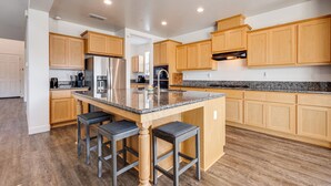 A modern kitchen with wooden cabinets, a granite countertop, and a central island with bar stools. - 1 Mi to Golf! Spacious & Modern Home in Dinuba (Dinuba)