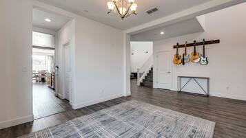 A spacious hallway with a chandelier, a rug, and guitars on a stand.