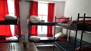 A dormitory room with bunk beds, a table with bottles, and a window with red curtains. - A Shared room simpel basic with bunkbeds you have to bring your own r sleeping (Utrecht)