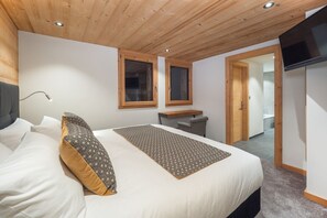Une chambre à coucher avec un lit, deux fenêtres, un bureau et un téléviseur.