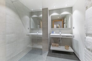 Une salle de bain moderne avec deux lavabos, une douche et un miroir.