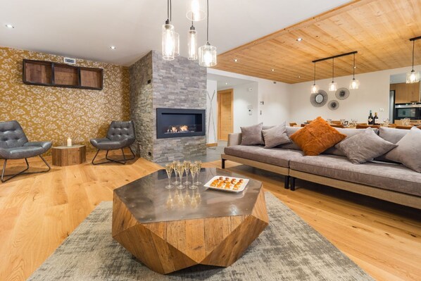 Un salon moderne doté d’une cheminée en pierre, d’un plafond en bois et d’un coin repas avec un canapé et une table.