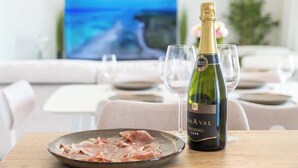 Et spisebord med cava, en tallerken mad og glas, med et fjernsyn der viser et naturskønt udsigt.