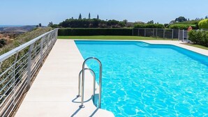 En rektangulær swimmingpool med en metalstige, omgivet af et hvidt hegn, og et frit udsyn til landskabet.