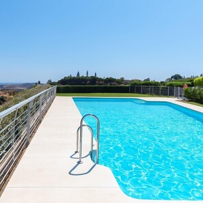 A rectangular swimming pool with a metal ladder, surrounded by a white fence, and a clear view of the landscape.