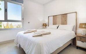 A bedroom with a large bed, two bedside tables, a window with a view, and a wooden headboard.