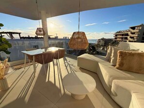 Una terraza en la azotea con una mesa de comedor, sillas, un sofá y lámparas colgantes de ratán.