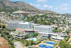 Un hotel con varias edificaciones, una piscina y montañas al fondo.