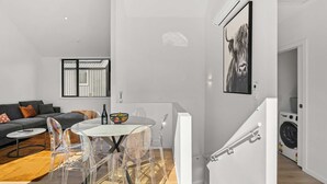 A modern living space with a dining area, a gray sofa, a clear glass table, and a staircase leading to a laundry area. - Central Escape - A modern townhouse with mountain and lake views in the heart of Queenstown. (Queenstown)