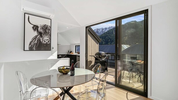 A modern kitchen with a large window, a dining area with a glass table, and a view of mountains. - Central Escape - A modern townhouse with mountain and lake views in the heart of Queenstown. (Queenstown)