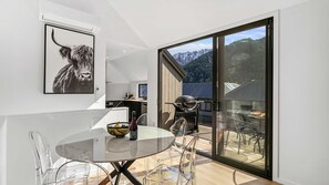 Eine moderne Küche mit einem großen Fenster, einem Essbereich mit einem Glastisch und Blick auf Berge.