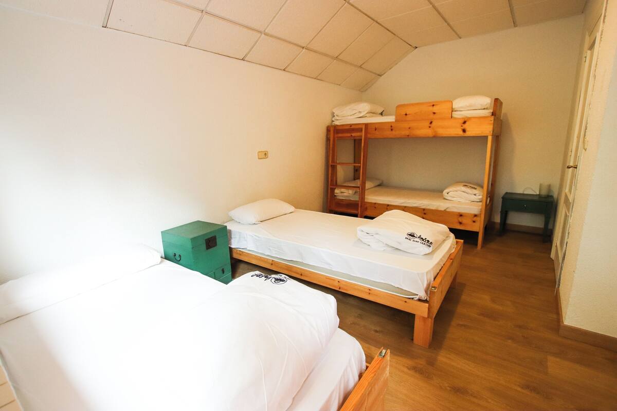 A small, cozy room with two single beds, a bunk bed, and a green storage box.